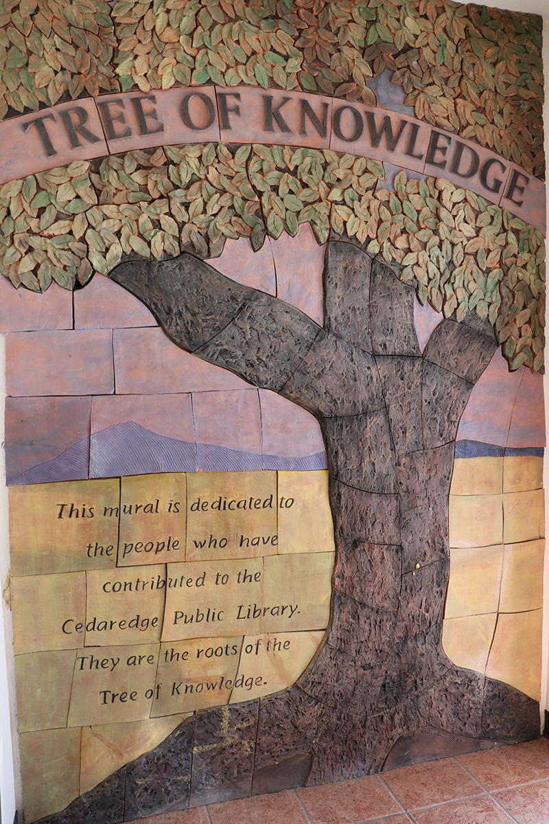 A textured mural of a tree greets patrons as they enter the library. Through the middle of the tree are the words "Tree of Knowledge".