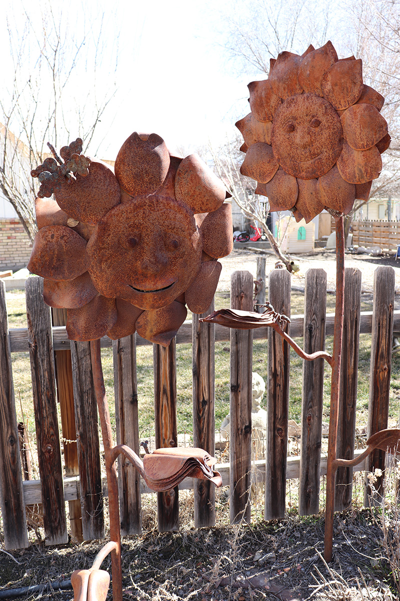 Smiling metal sunflowers peak out of the garden bushes.
