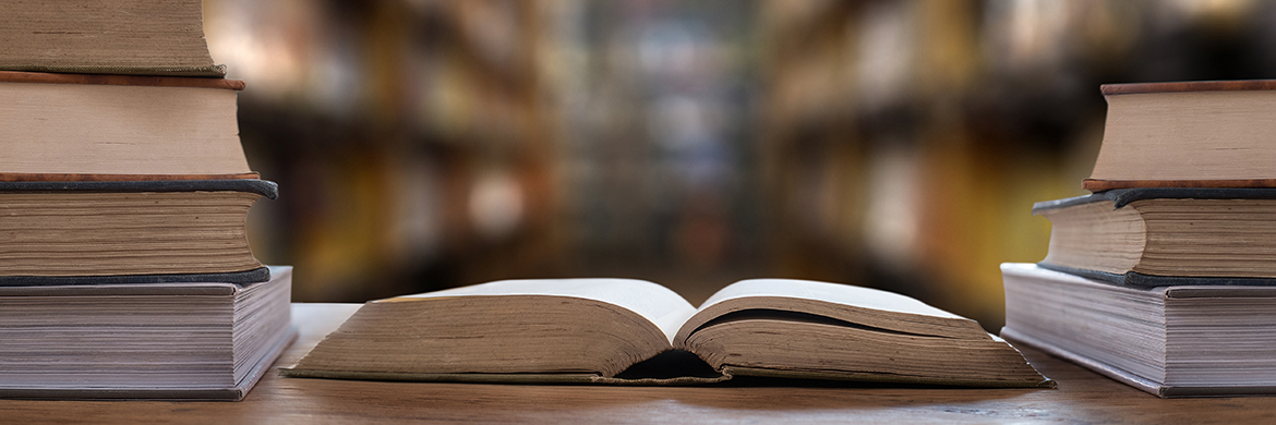 Open book sitting on a desk with stacks of books on either side