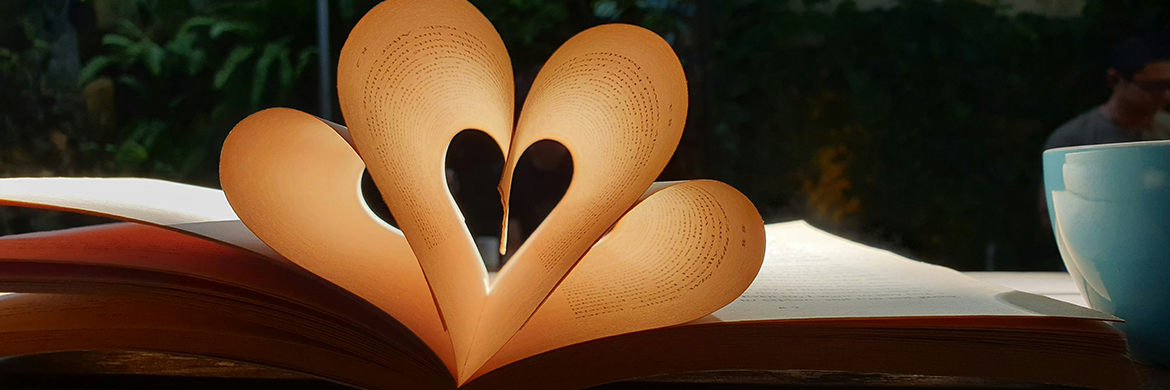 An open book with pages curled inward to create a heart sha[e