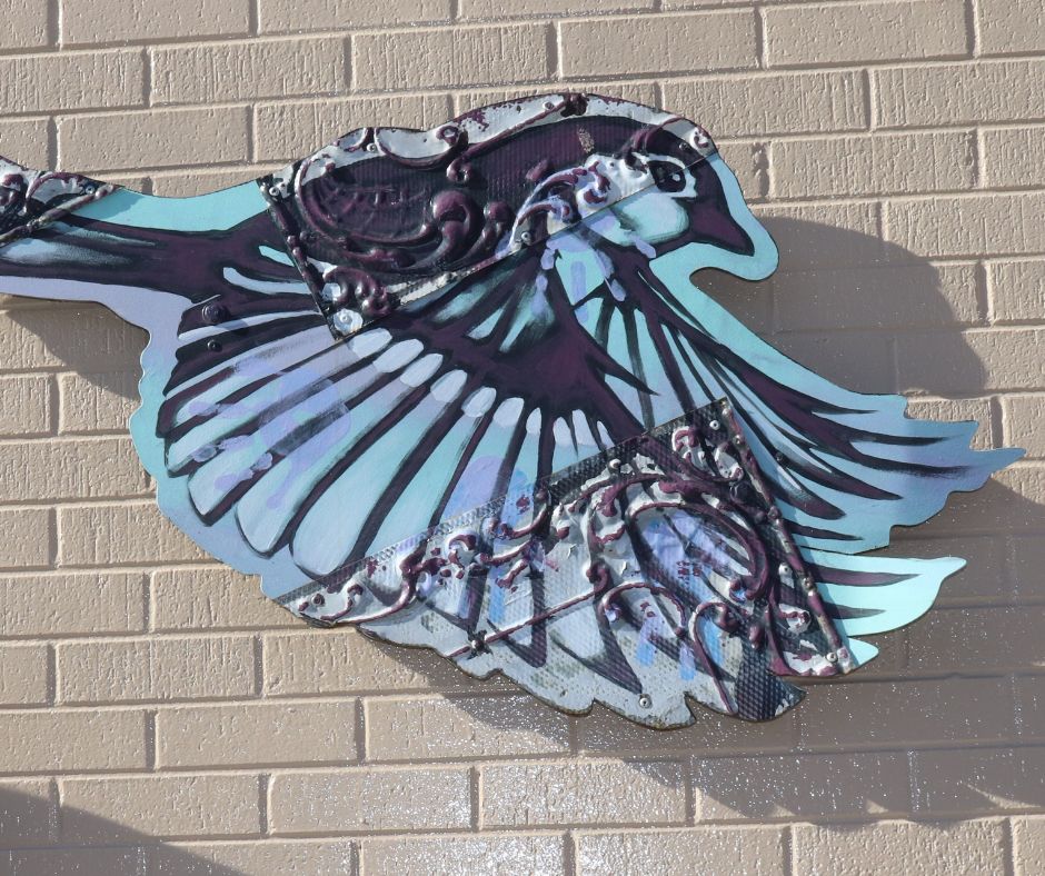 A blue and purple metal bird, adorns a cream colored brick wall.