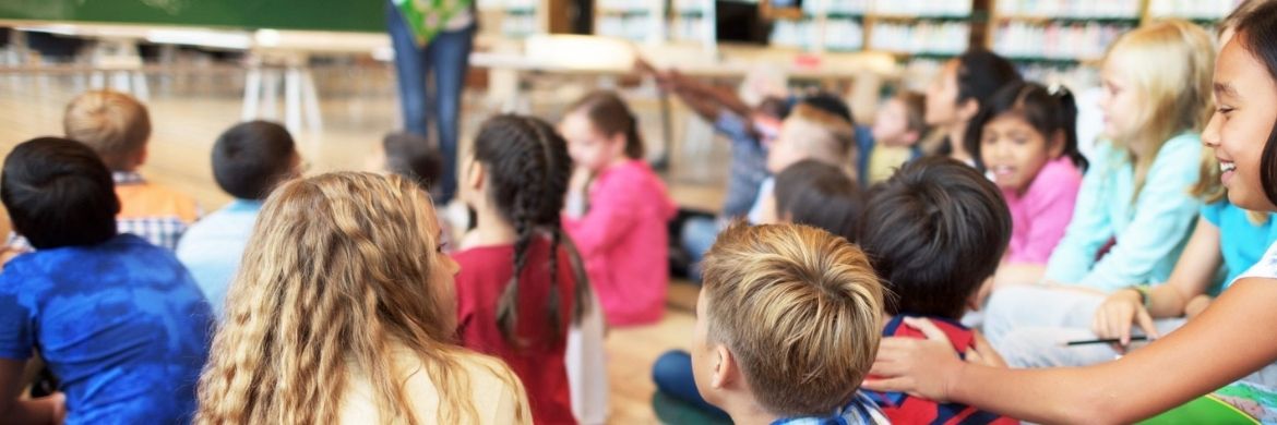 Several elementary-aged children looking to a teacher for instruction