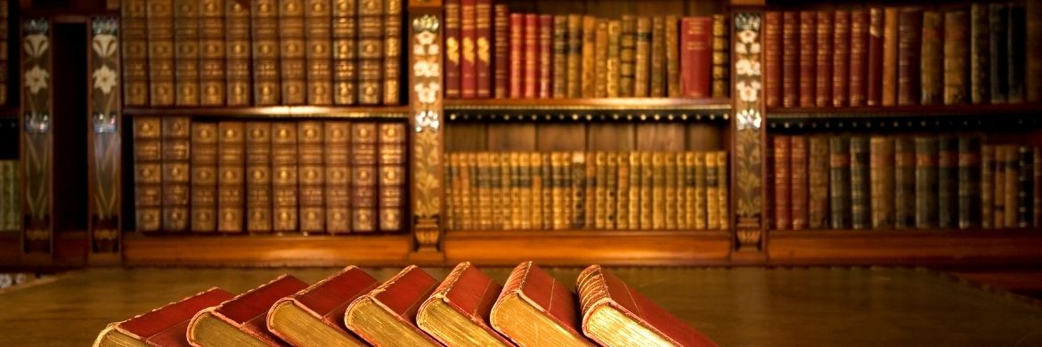 Several legal texts rest on a table. The background is a library filled with volumes of texts.