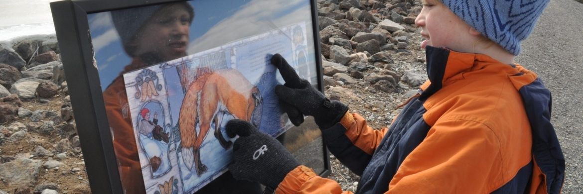 A young boy, wearing winter clothes, examines a StoryWalk panel.