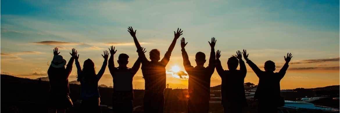 Several people rejoicing and silhouetted by a setting or rising sun. 
