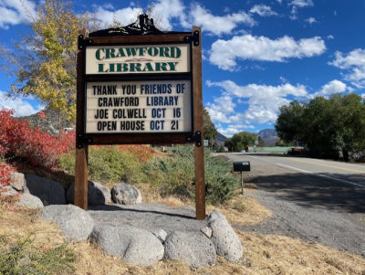 Wooden "Crawford Library" sign by road advertising upcoming events
