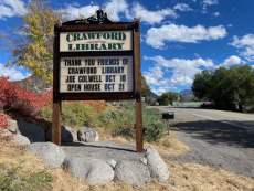 Wooden "Crawford Library" sign by road advertising upcoming events