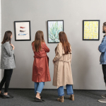 Several people stand looking at various art pieces that are hung on the wall.