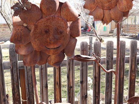 Smiling metal sunflowers peak out of the garden bushes.