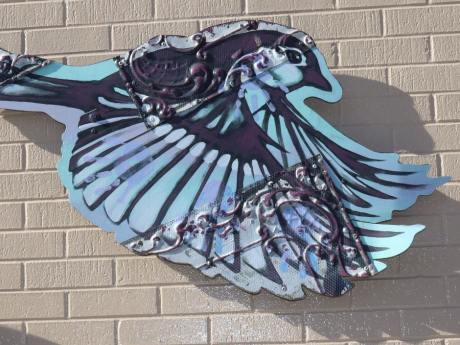 A blue and purple metal bird, adorns a cream colored brick wall.