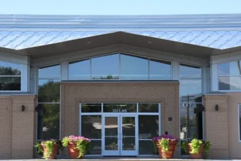 Glass and brick front entrance of the Delta Public Library with colorful planters outside the door