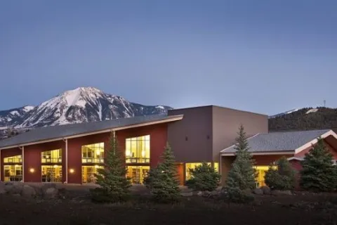Lit up windows of the Paonia Library building with mountains and sky in background