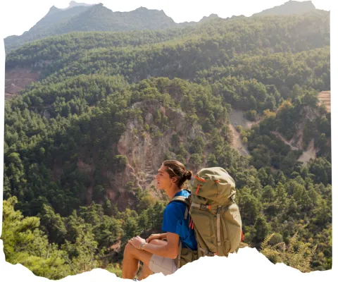 A person with a large backpack is resting, with mountain scenery.
