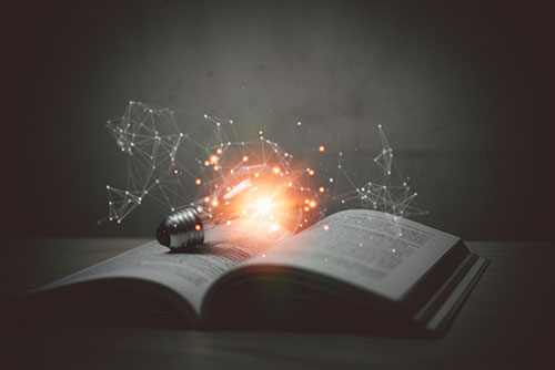 A lit up light bulb laying on top of an open book